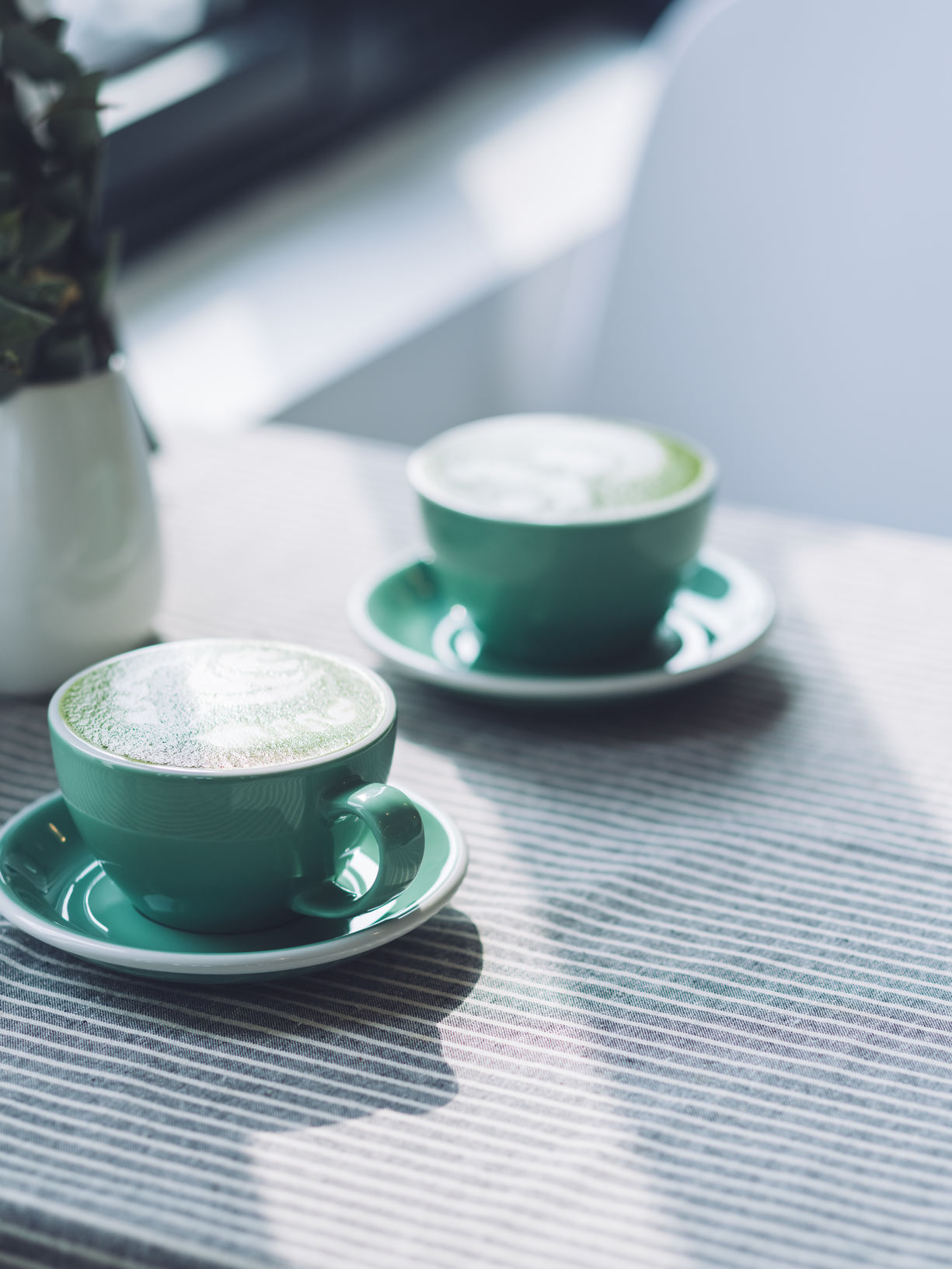 Interior gallery - 9 of 11 - Two Cups Of Coffee With Steam Milk In Green Cups On Table Against Sunlight